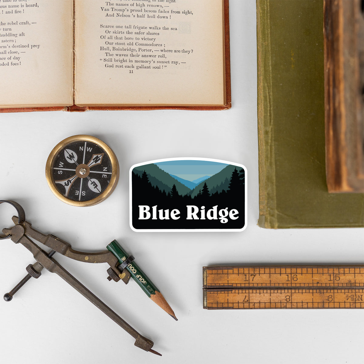 Laid among a compass, pencil, ruler, and open book, the Blue Ridge sticker sits on a white tabletop.