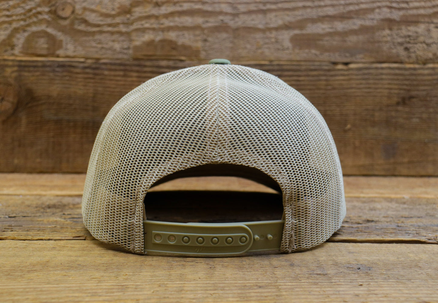 From behind on wooden boards, the Bigfoot Peace trucker hat opens to its snap strap under cream mesh.