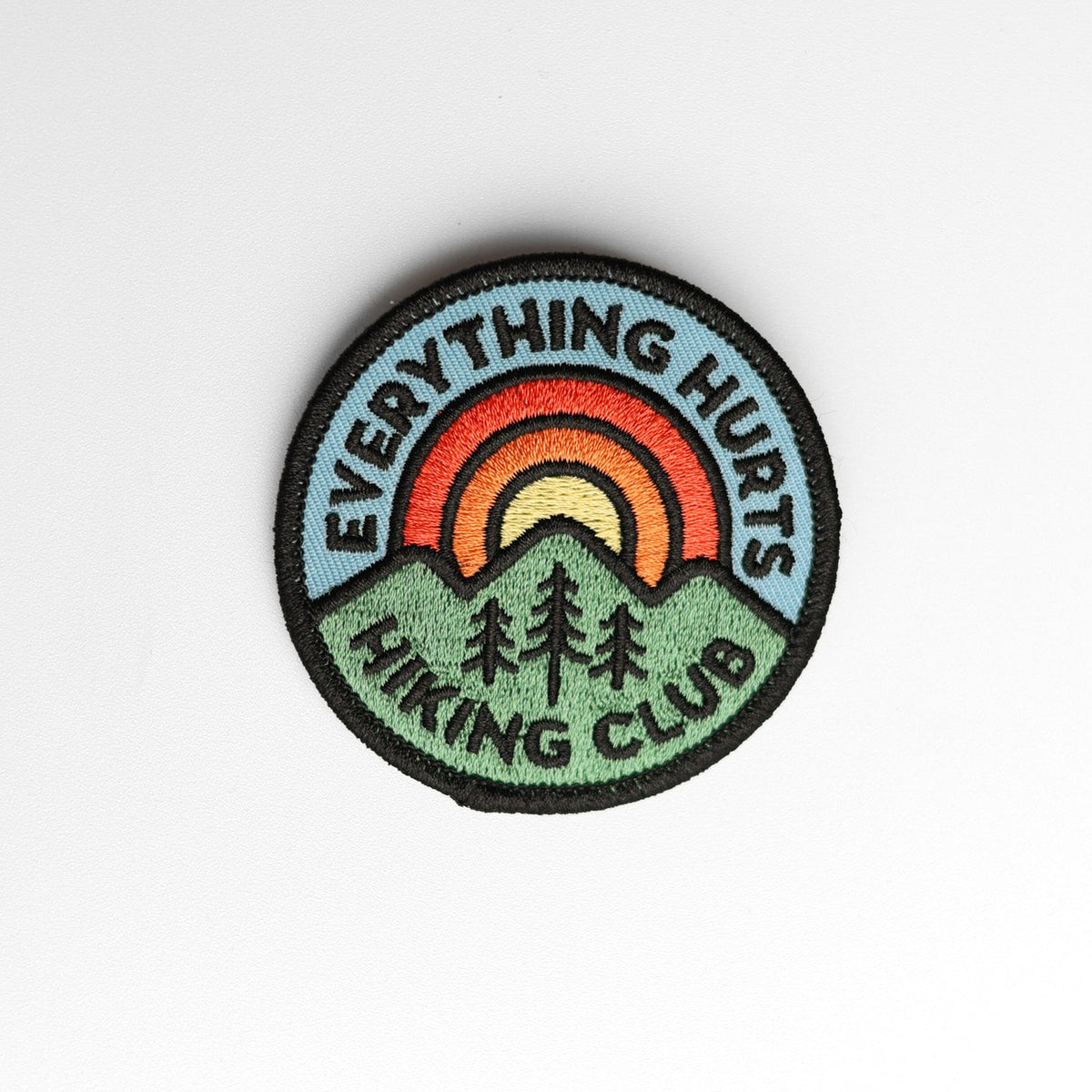 Slightly textured paper backs the Everything Hurts Hiking Club patch, three embroidered trees below the sun.