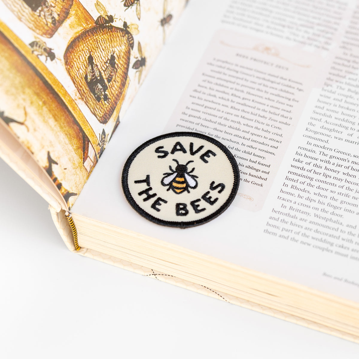 Resting on a bee illustrated book page, the round Save The Bees patch sits near the spine's cream edge.