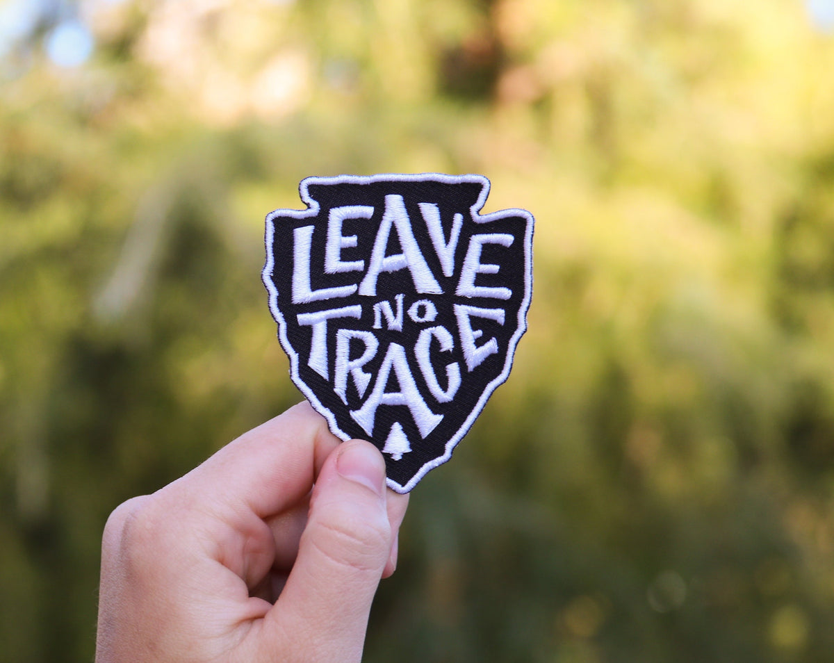 Held toward the sky, the Leave No Trace patch stands bright over sunlit trees.