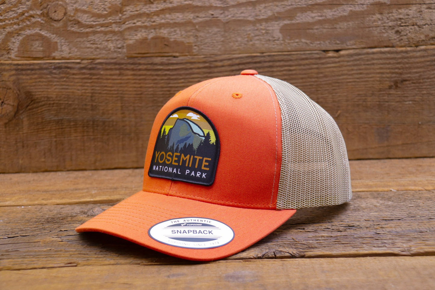 Against grey barn boards, the orange Yosemite National Park trucker hat shows off its khaki mesh back.