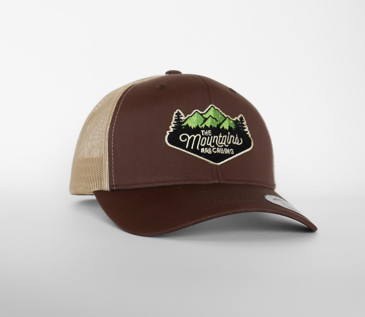 Rich brown twill and tan mesh on the Mountains Are Calling trucker hat, patch script clear up close.