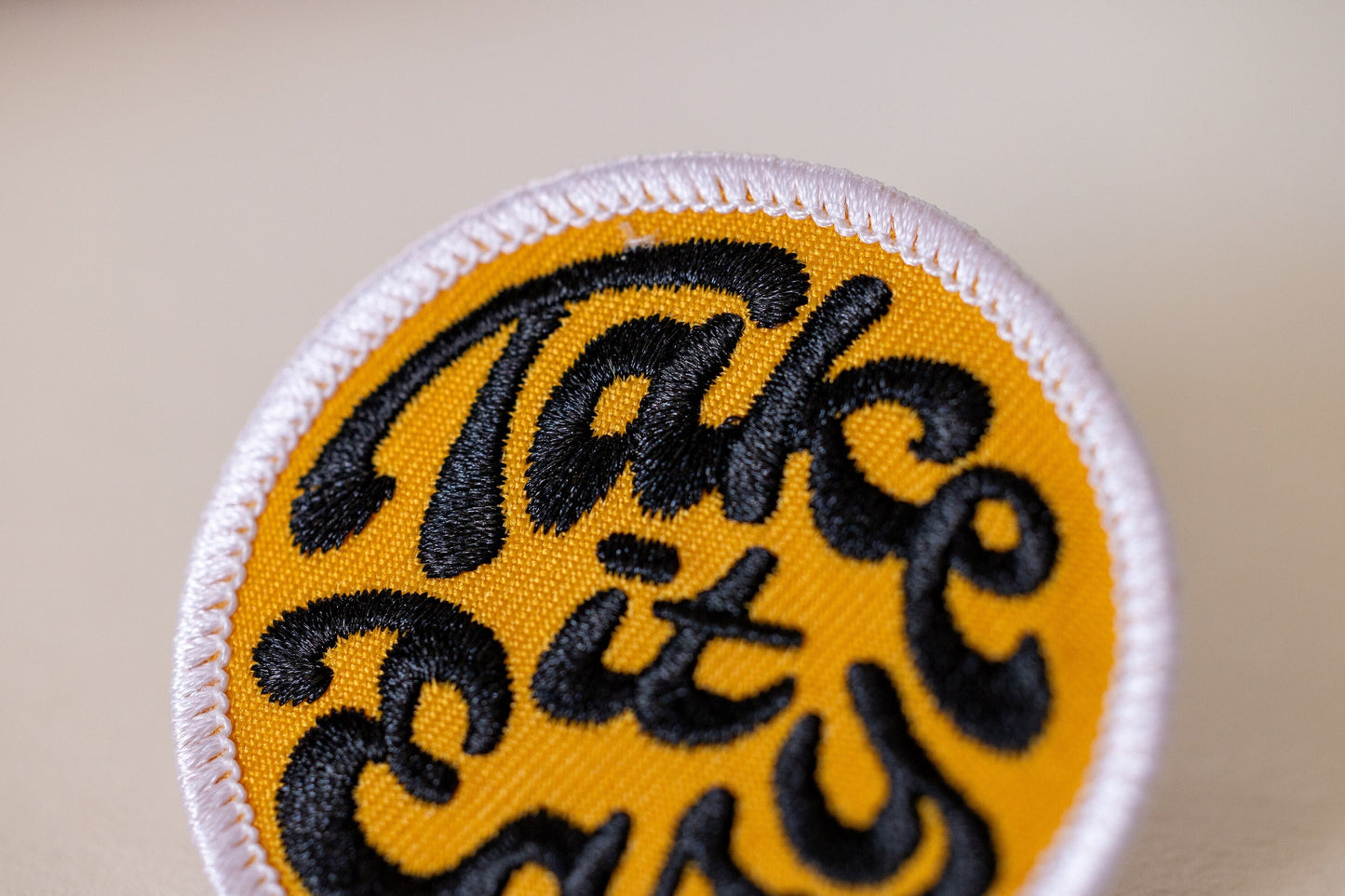 Cropped tight against a tan background, the yellow Take it Easy patch reveals its raised black stitching.