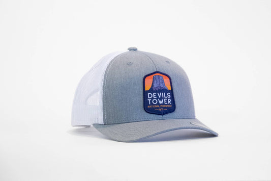 Heather grey and white Devils Tower National Monument trucker hat angled to show its sunset patch on the front panel.