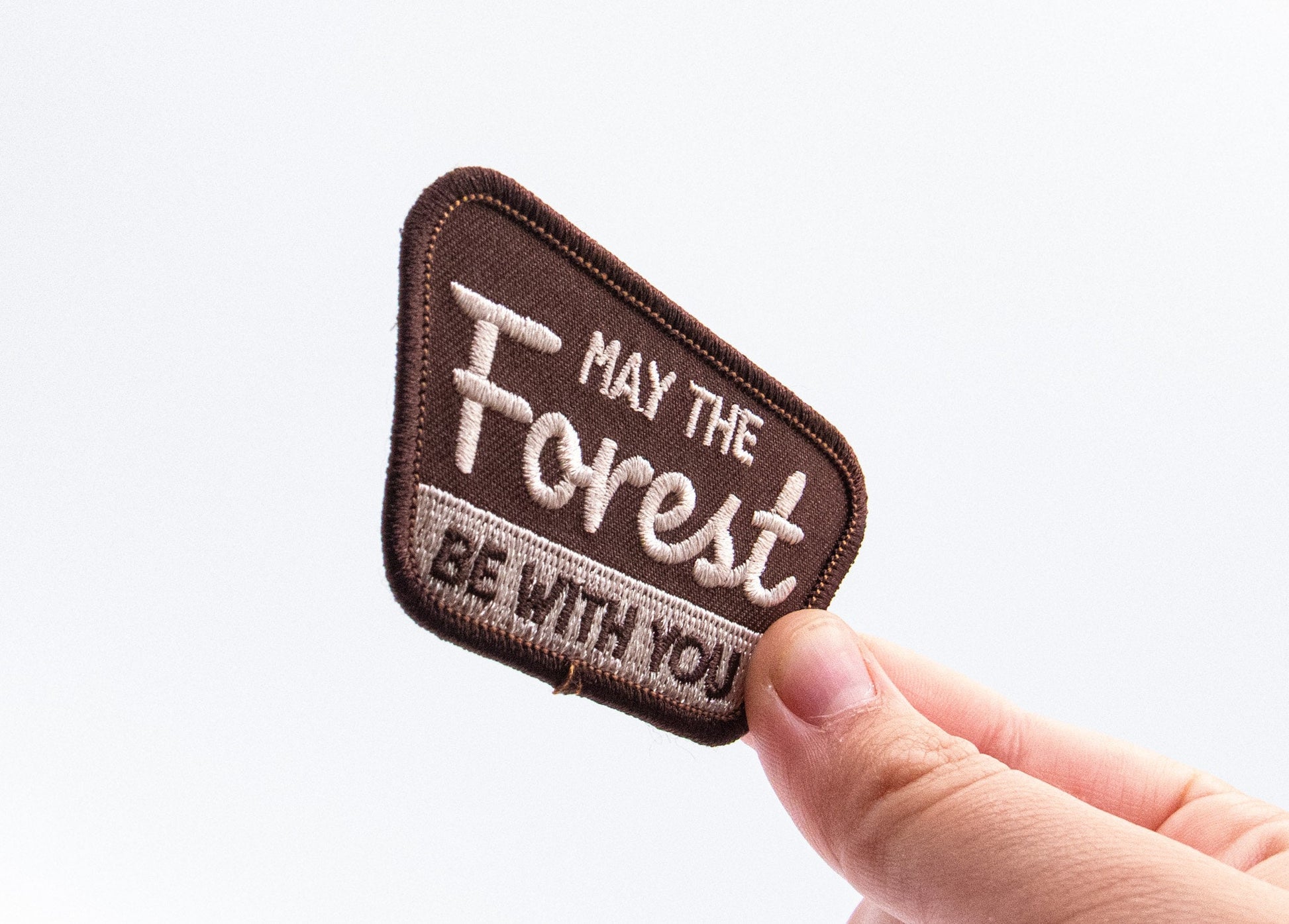 Angled toward the camera between finger and thumb, the May The Forest Be With You patch catches soft light.