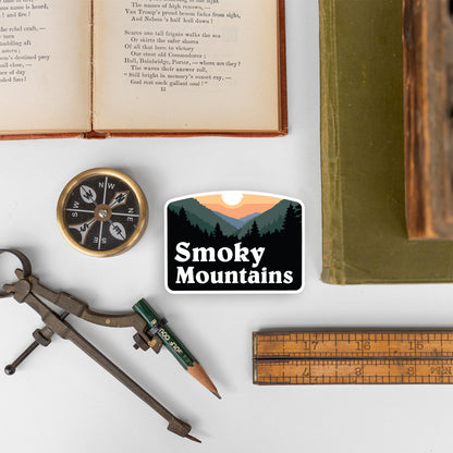The Smoky Mountains sticker rests among a compass, ruler, drafting tool, and an open antique book.