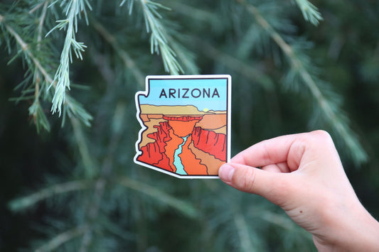 Backed further off against the same evergreen branches, the Arizona sticker shows its river cutting red cliffs.