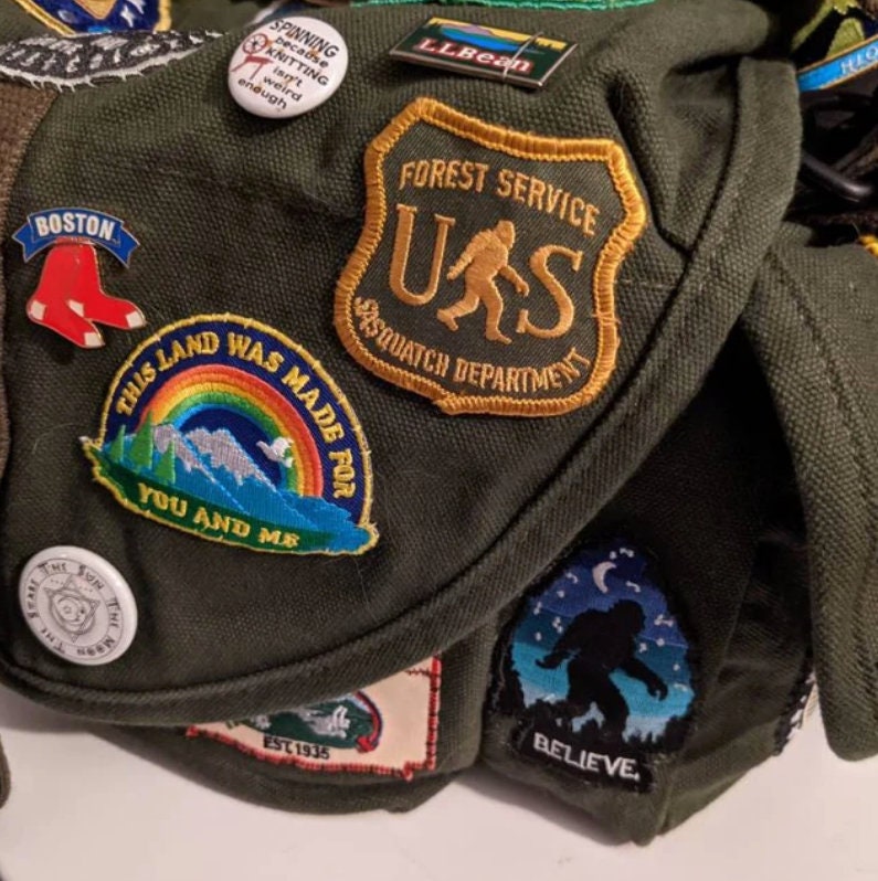 On a jacket crowded with pins and patches, the US Sasquatch Department patch takes the center spot.