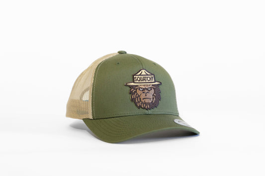 Olive and tan Bigfoot Squatchy trucker hat sits on a white backdrop with its ranger patch facing forward.