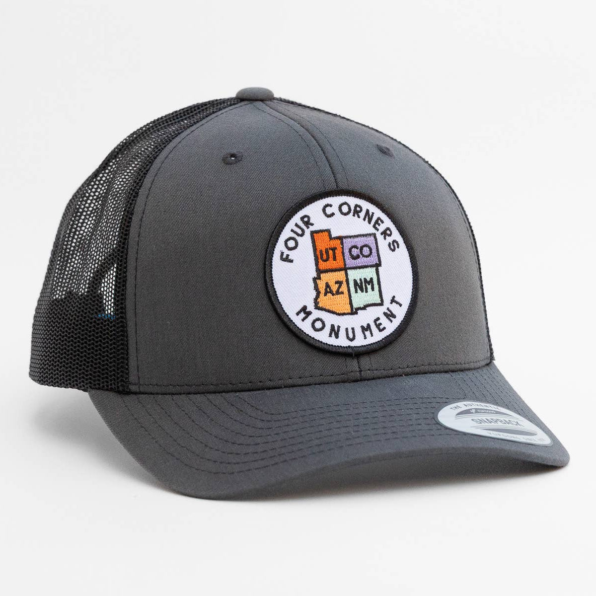 Charcoal front and black mesh on the Four Corners Monument trucker hat, round state patch centered above the brim.