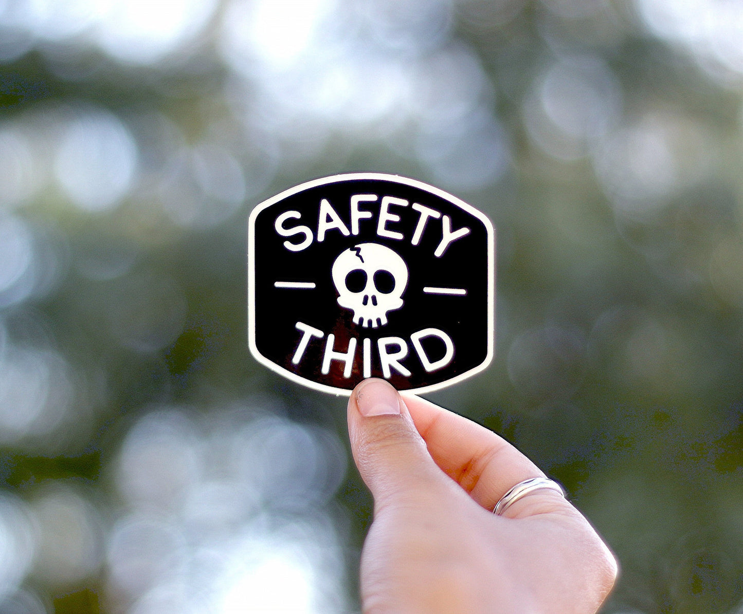 Raised toward a canopy of trees, the Safety Third sticker glows against soft round bokeh.
