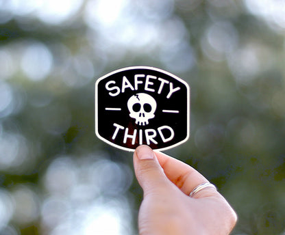 Raised toward a canopy of trees, the Safety Third sticker glows against soft round bokeh.