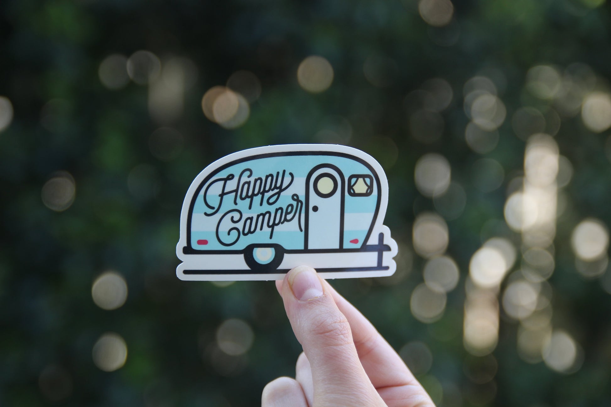 Held at arm's length in dim woods, the Happy Camper sticker shows its round window and tiny red trim.