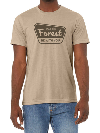 A man in blue jeans wears the tan May The Forest Be With You t shirt with its brown badge print.