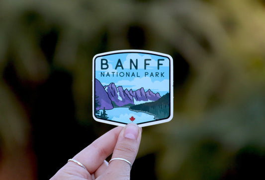 Held farther back against blurred green foliage, the Banff National Park sticker shows its full crest shape.