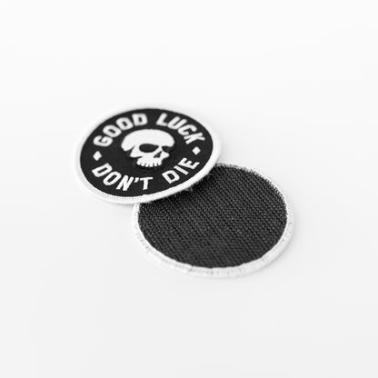 One Good Luck Don't Die patch rests face up while a second behind it shows its plain black fabric backing.