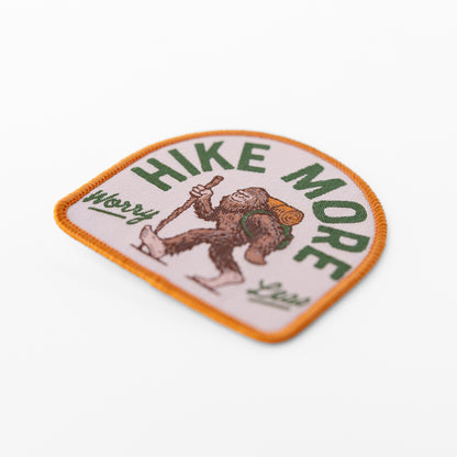 Angled to show its orange border and stitched texture, the Hike More Worry Less patch catches light across Bigfoot's figure.