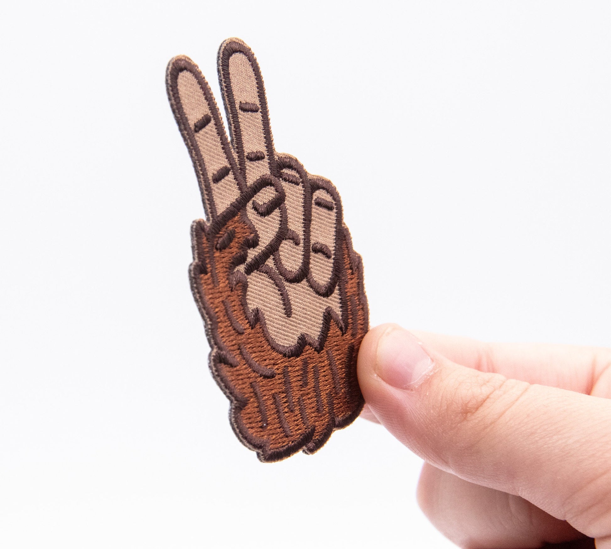 Pinched sideways between thumb and finger, the Bigfoot Peace Patch shows its stitched edge and slight curve.