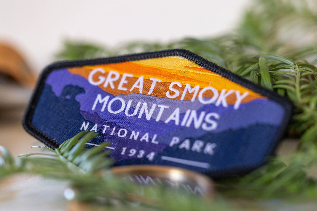 Close in among evergreen sprigs, the Great Smoky Mountains patch leans past a brass ring gone soft in blur.