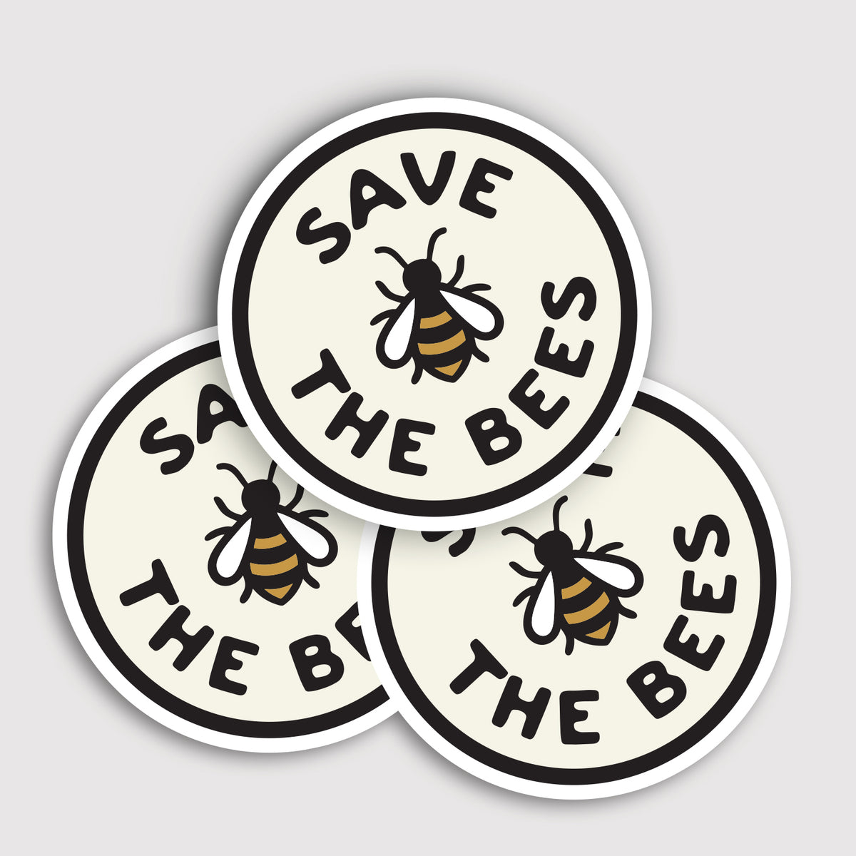 Three Save The Bees stickers overlap in a small pile, their bee icons facing different directions.