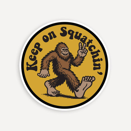 Round gold Keep on Squatchin' sticker with a peace sign Bigfoot mid stride, shown flat on plain white.