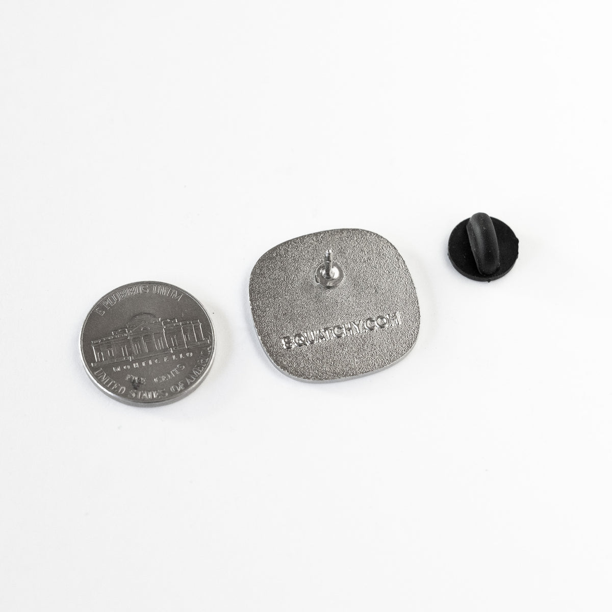 Turned to its back, the Everything Hurts enamel pin reveals its pin post and rubber clasp beside a nickel for scale.