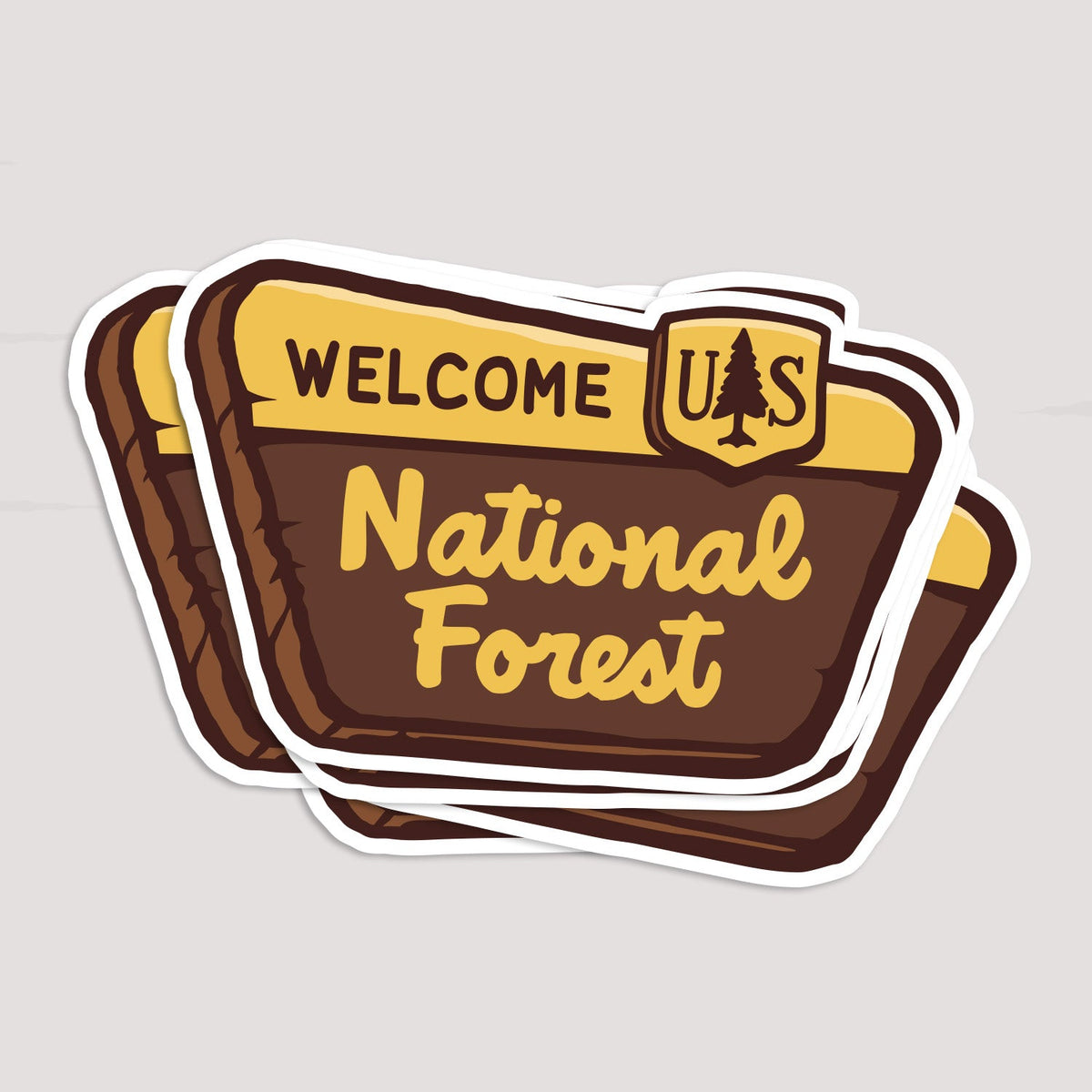 Two National Forest Sign stickers overlap in a small stack on a pale grey surface.