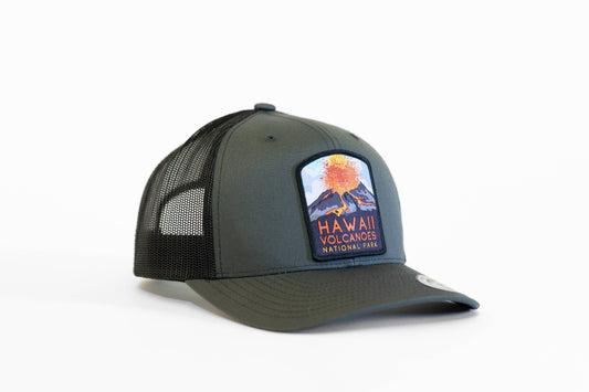 Angled on white, the dark green Hawaii Volcanoes National Park trucker hat shows its erupting volcano patch.