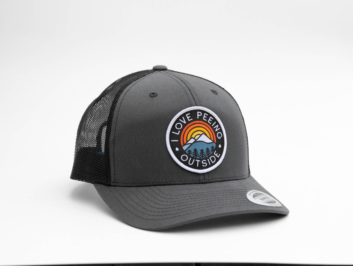 Charcoal grey I Love Peeing Outside trucker hat pairs black mesh sides with the circular sunset patch.