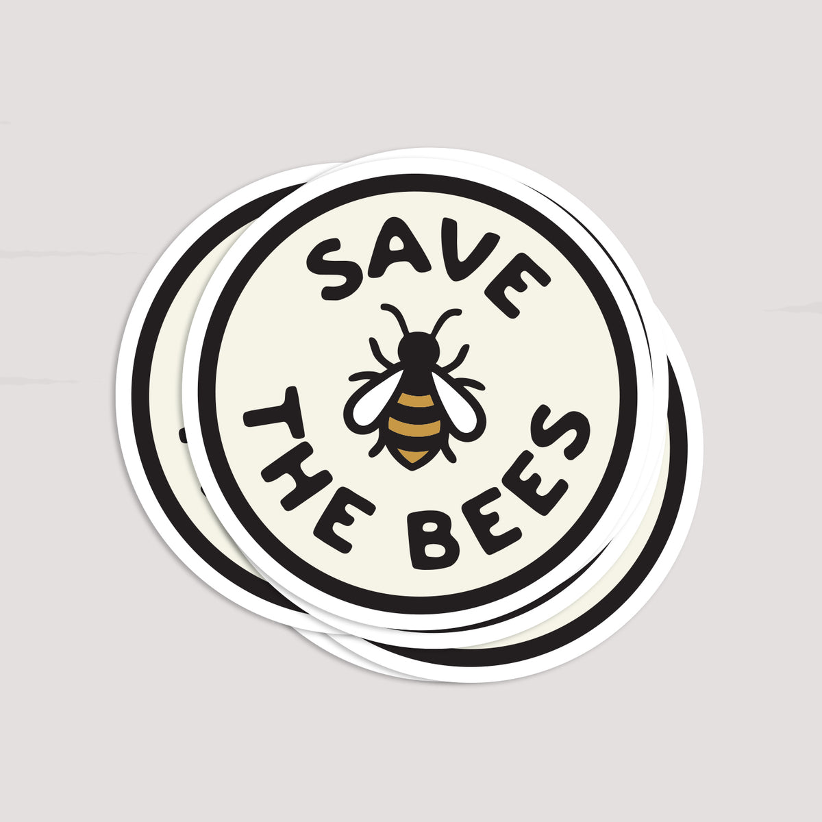 Several Save The Bees stickers lie fanned in a loose stack, each round edge overlapping the next.