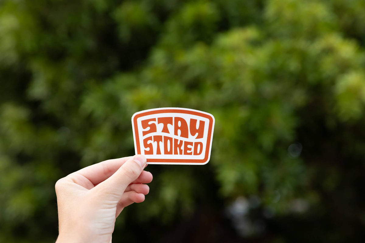 Raised against a leafy green tree, the Stay Stoked sticker shows its rounded block lettering.