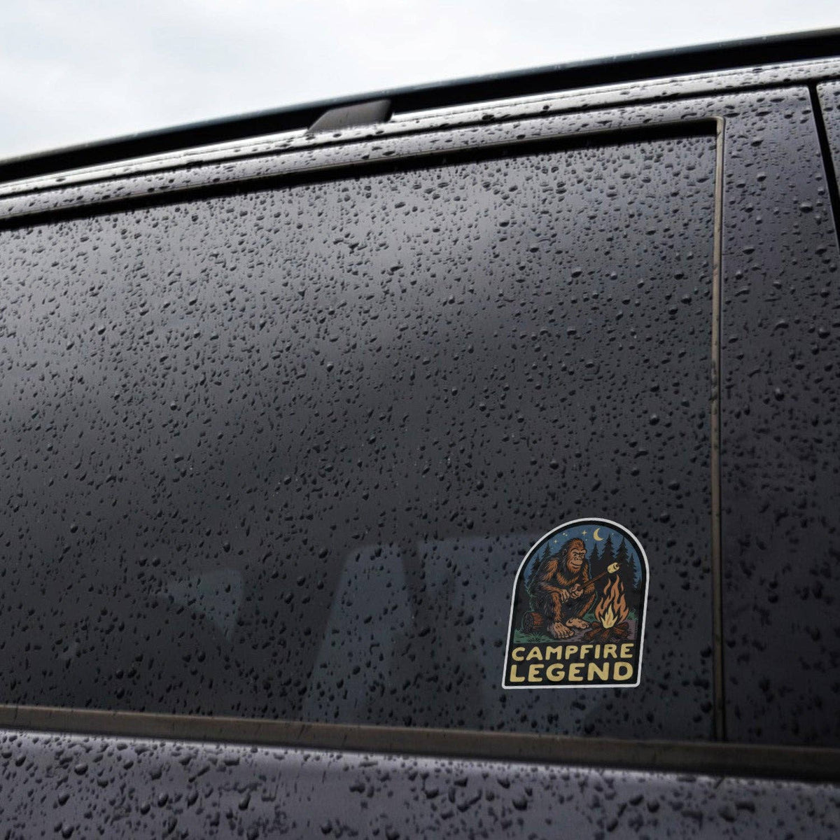 Stuck to a rain beaded black car window, the Campfire Legend sticker keeps its colors under the water drops.