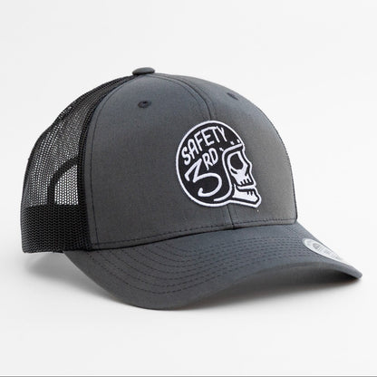 Closer angle on the charcoal Safety 3rd Helmet trucker hat, stitching visible around the embroidered skull patch.