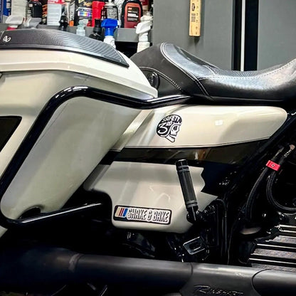 On the cream side panel of a motorcycle in a garage, the Safety 3rd Helmet sticker rides above the engine.
