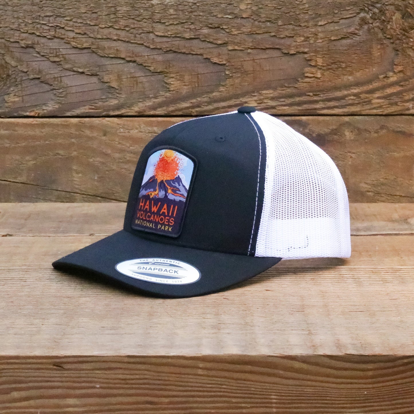 Turned three quarters on a wood plank, the Hawaii Volcanoes trucker hat shows its snapback brim label.