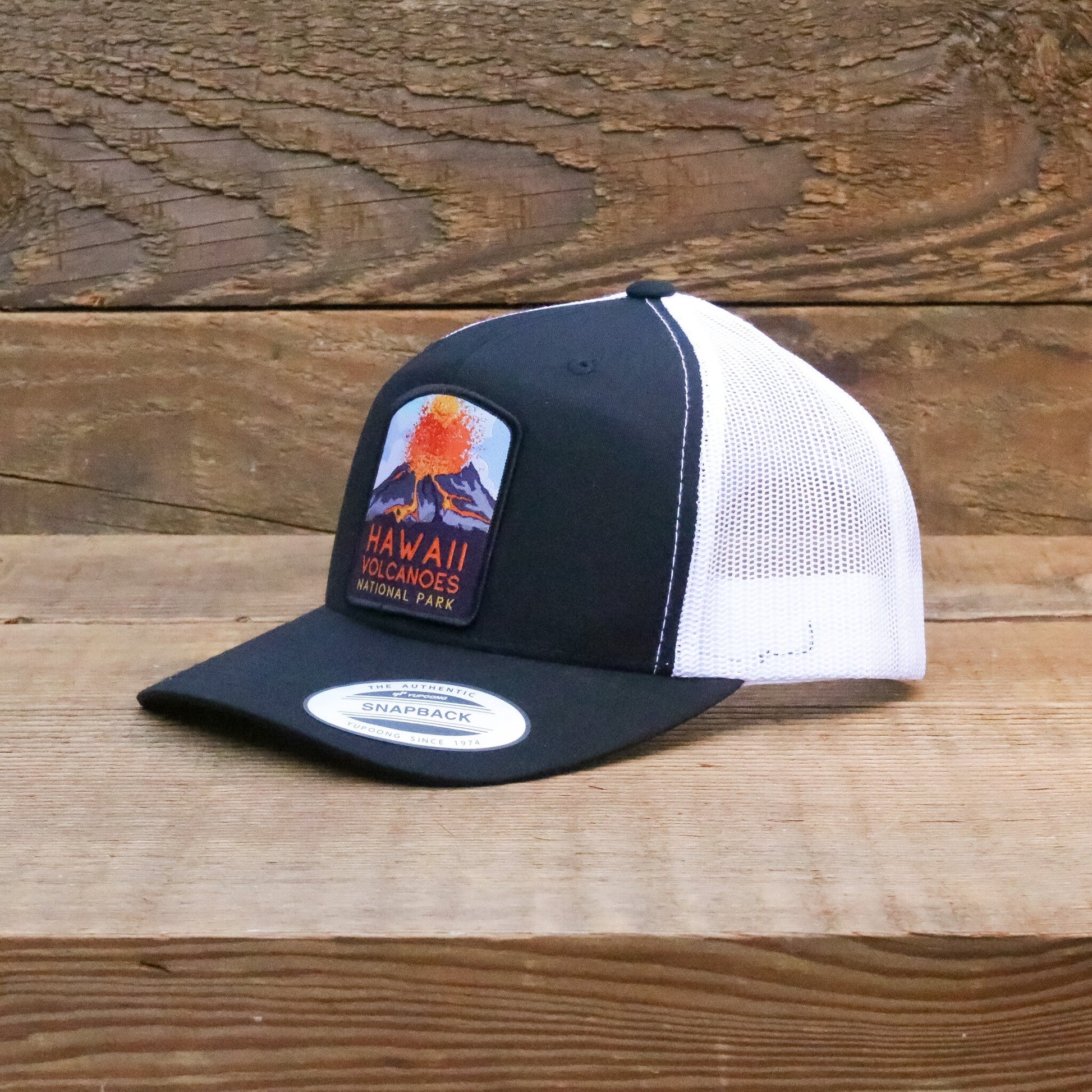 Turned three quarters on a wood plank, the Hawaii Volcanoes trucker hat shows its snapback brim label.