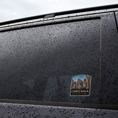 Raindrops cover a dark car window where the Chiricahua National Park sticker clings near the lower corner.