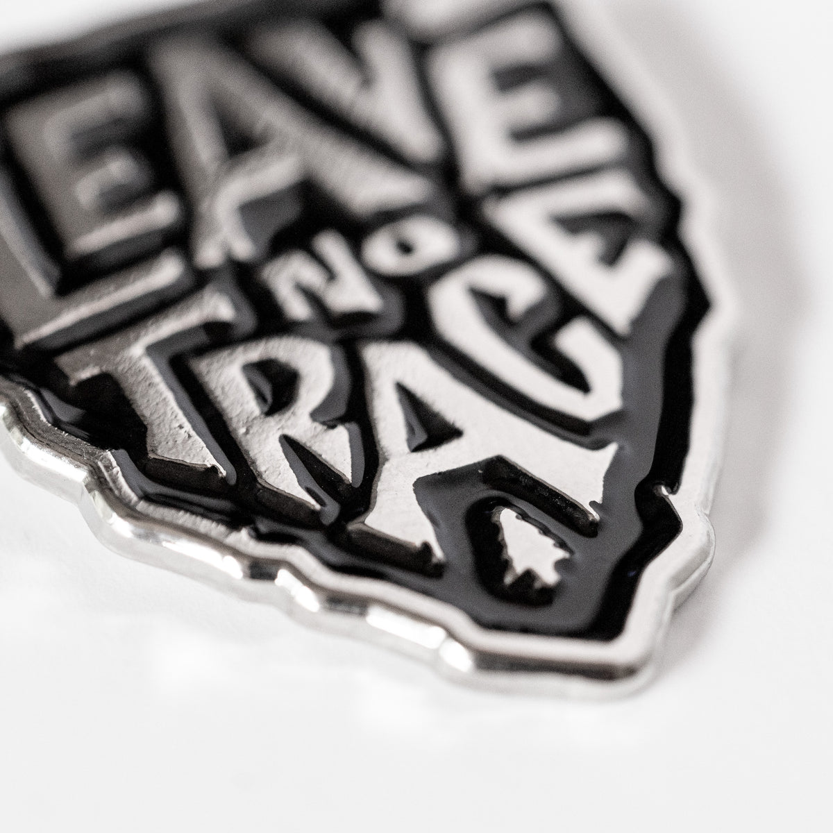 A close angle on the Leave No Trace pin catches light along its raised silver letters and black enamel.