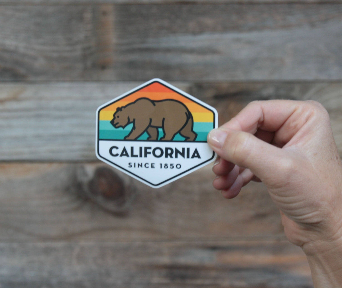 Against weathered grey barn boards, the California State Bear sticker is pinched at one corner.