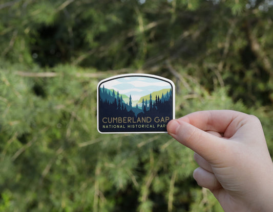 Held to one side against sunlit evergreens, the Cumberland Gap National Historical Park sticker shows its ridge and pines.