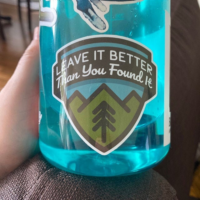 A blue water bottle filled with water wears the Leave It Better Than You Found It sticker indoors.