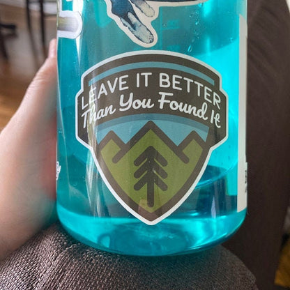 A blue water bottle filled with water wears the Leave It Better Than You Found It sticker indoors.