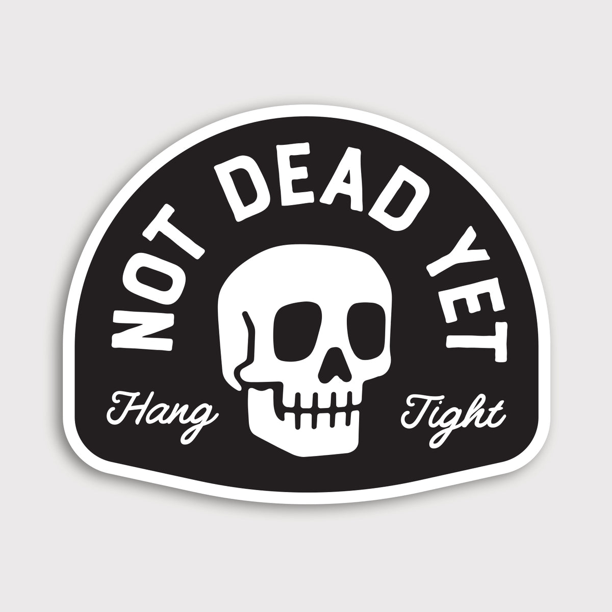 A white skull sits between arched Not Dead Yet lettering and a Hang Tight script on this black vinyl sticker.