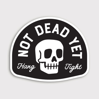 A white skull sits between arched Not Dead Yet lettering and a Hang Tight script on this black vinyl sticker.