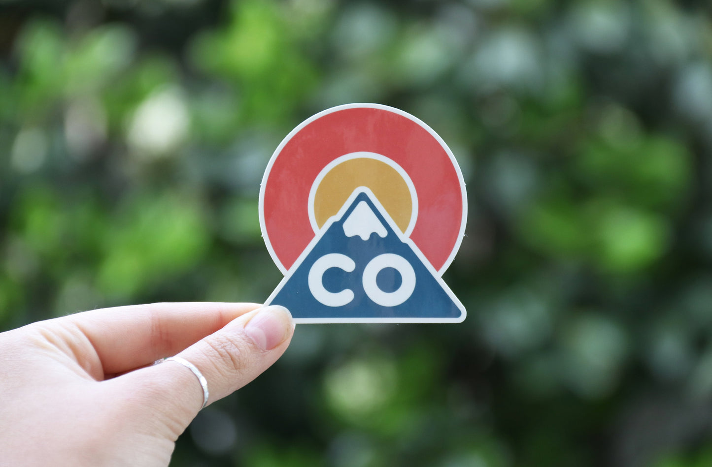 A wider frame catches the Colorado Triangle sticker pinched at one corner with soft green foliage behind.