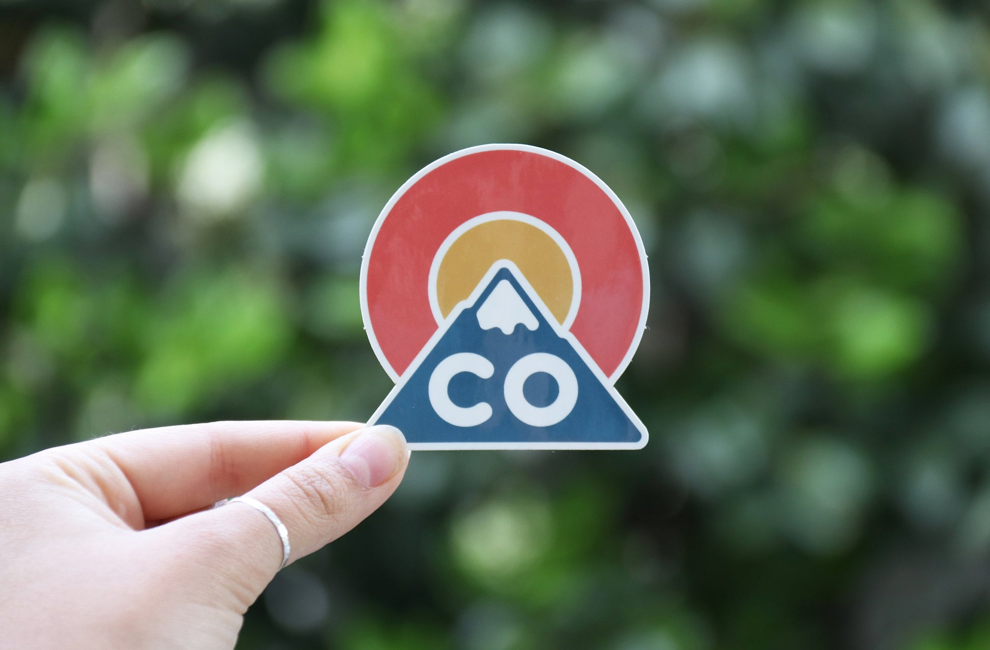A wider frame catches the Colorado Triangle sticker pinched at one corner with soft green foliage behind.