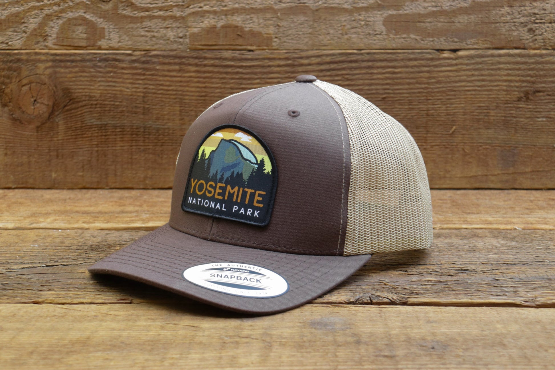 Brown and tan Yosemite National Park trucker hat propped against rough planks, brim label facing out.