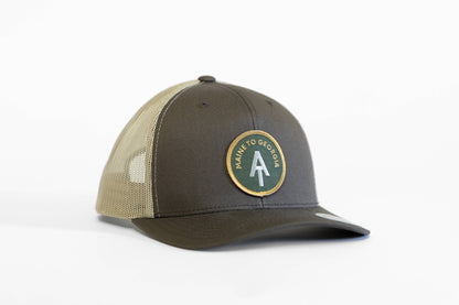 Brown crown with khaki mesh, the Appalachian Trail trucker hat turns its round green patch toward the camera.