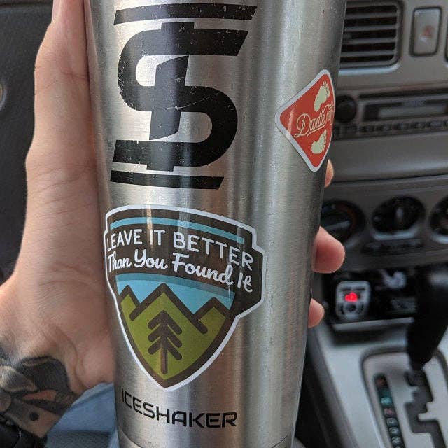 A steel Ice Shaker tumbler in a car carries the Leave It Better Than You Found It sticker.
